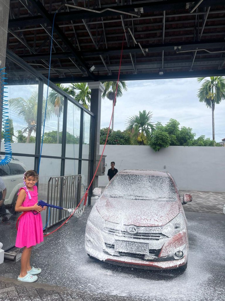 Anak perempuan kecil sedang belajar cuci mobil sendiri dengan busa salju